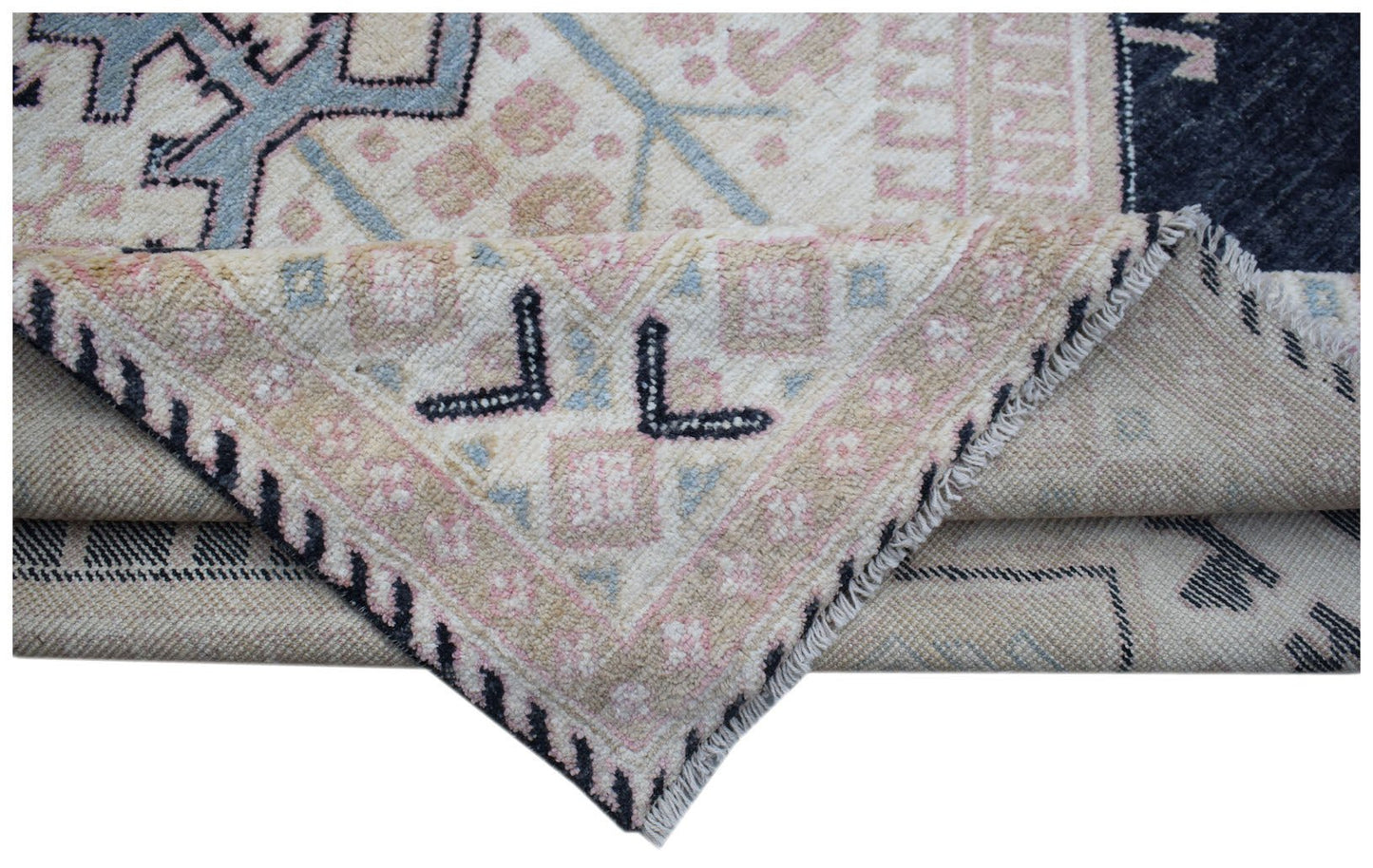 A corner of a handmade wool rug with a geometric pattern in blue, pink, and cream tones.