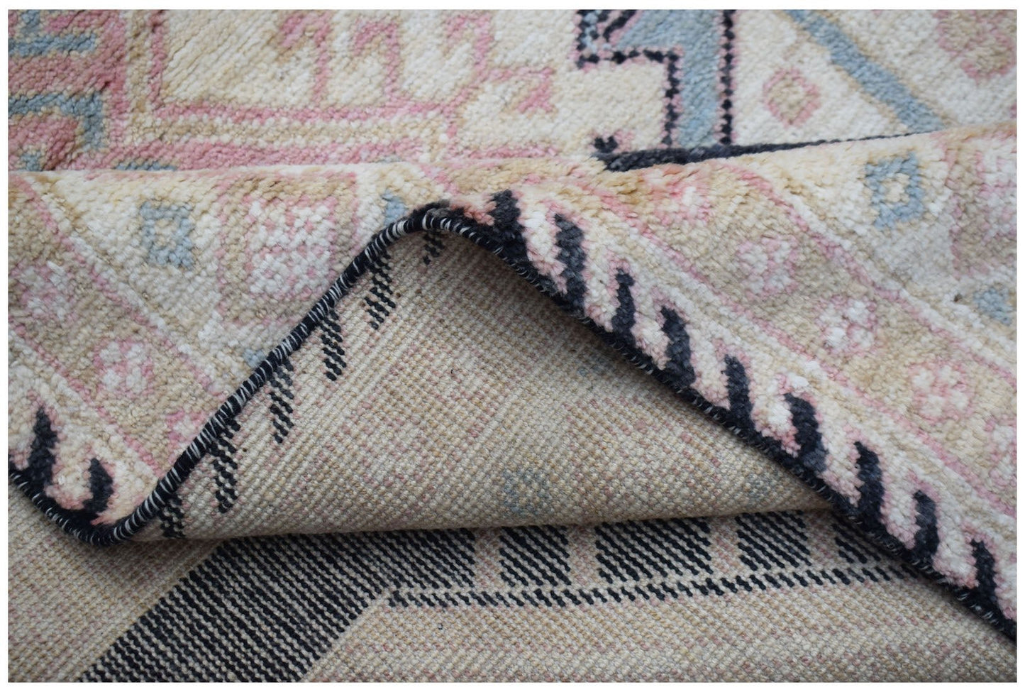 A close-up view of a handmade wool rug featuring a cream, pink, and blue geometric pattern.
