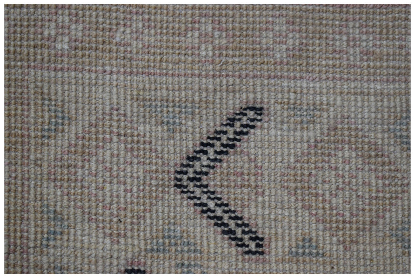 A close-up of a handmade wool rug featuring a beige background with a dark chevron pattern.