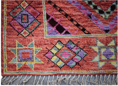 A hand-knotted wool rug featuring a vibrant red background with colorful geometric patterns.