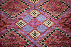 A hand-knotted wool rug featuring a vibrant geometric pattern in red, purple, and yellow.