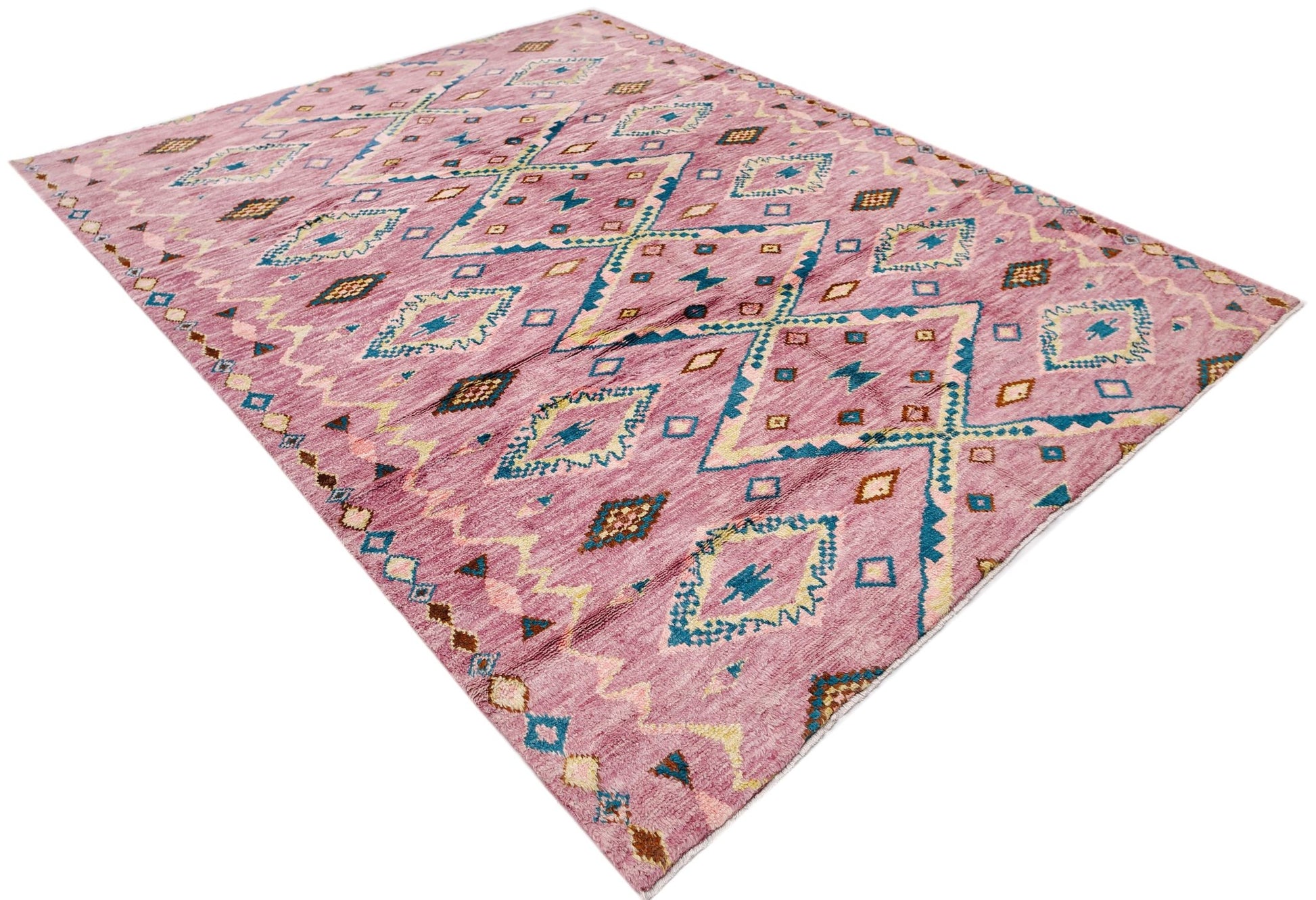 A handmade wool rug in a dusty pink hue featuring a geometric diamond pattern in blue and gold.