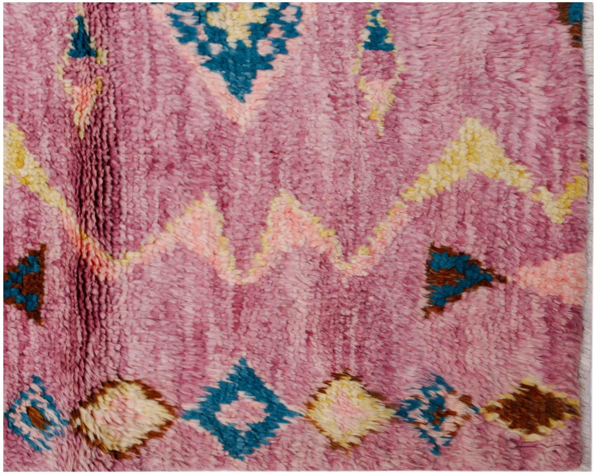 A handmade wool rug featuring a pink background with geometric patterns in blue, yellow, and brown.