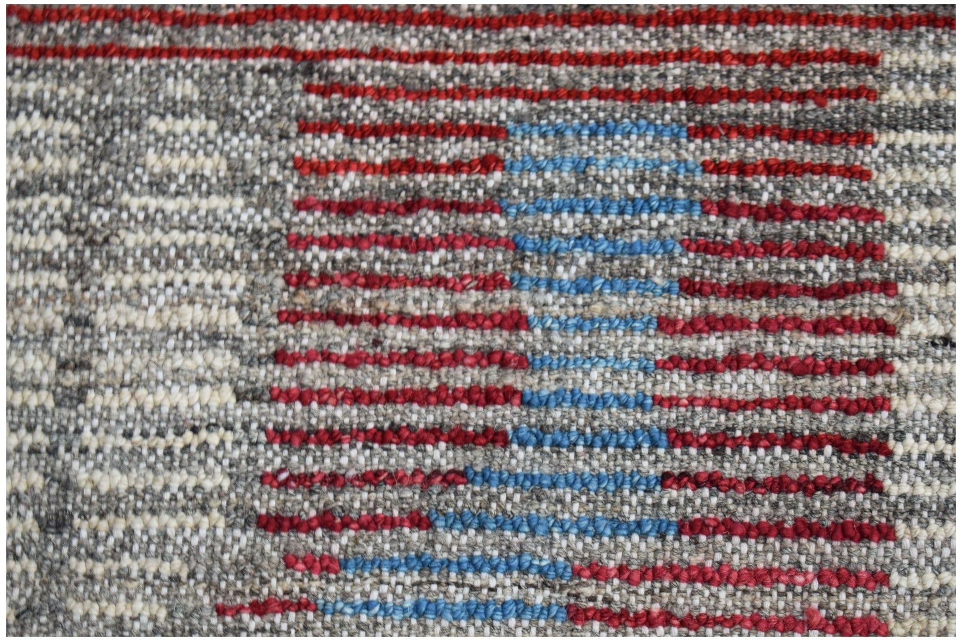 A hand-knotted wool rug featuring a textured pattern of horizontal red and blue stripes on grey.