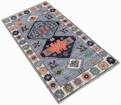 A rectangular handwoven wool rug featuring a grey field with geometric patterns in orange and blue.