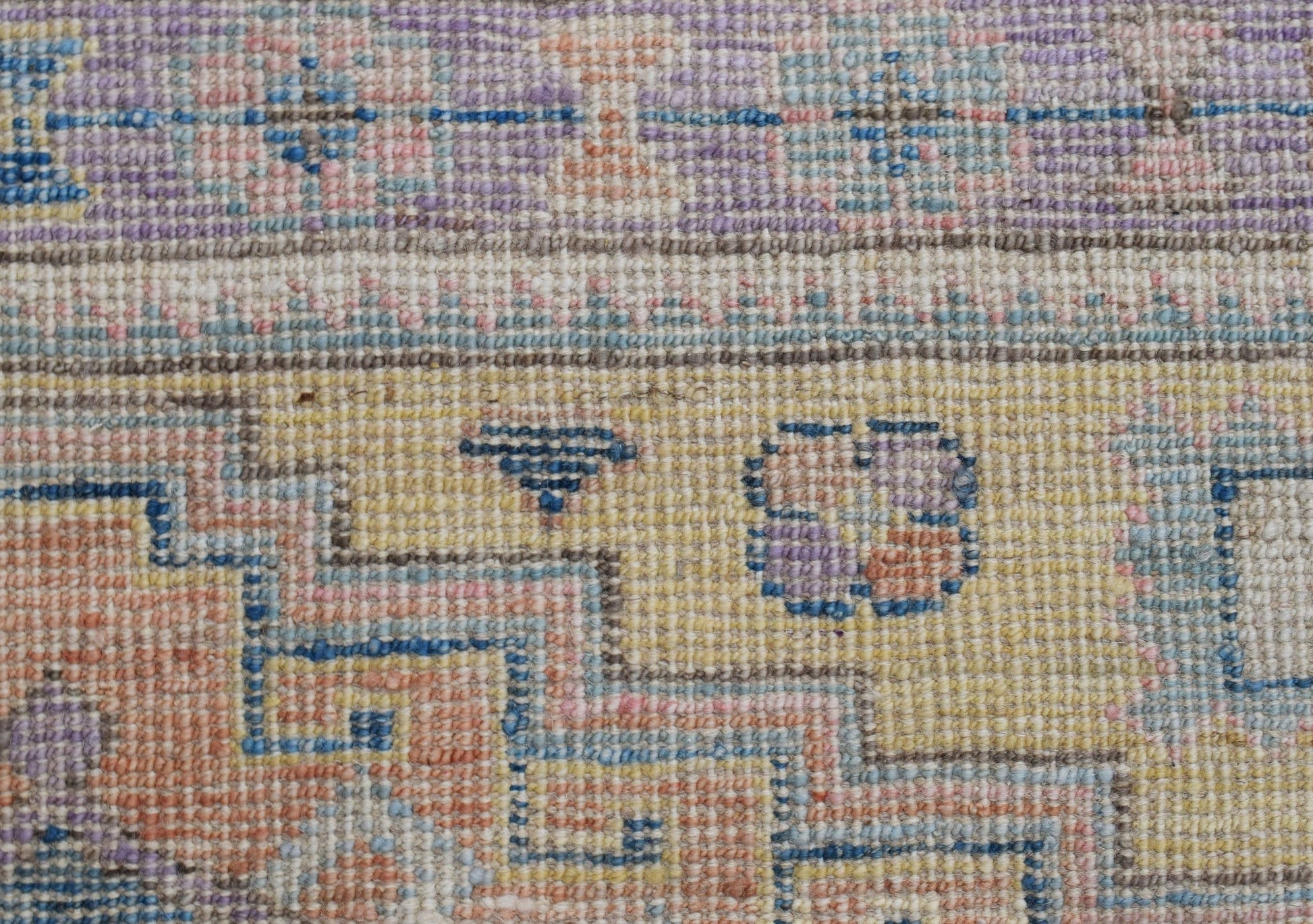 A close-up of a handwoven wool rug featuring a geometric pattern in soft pastel tones.