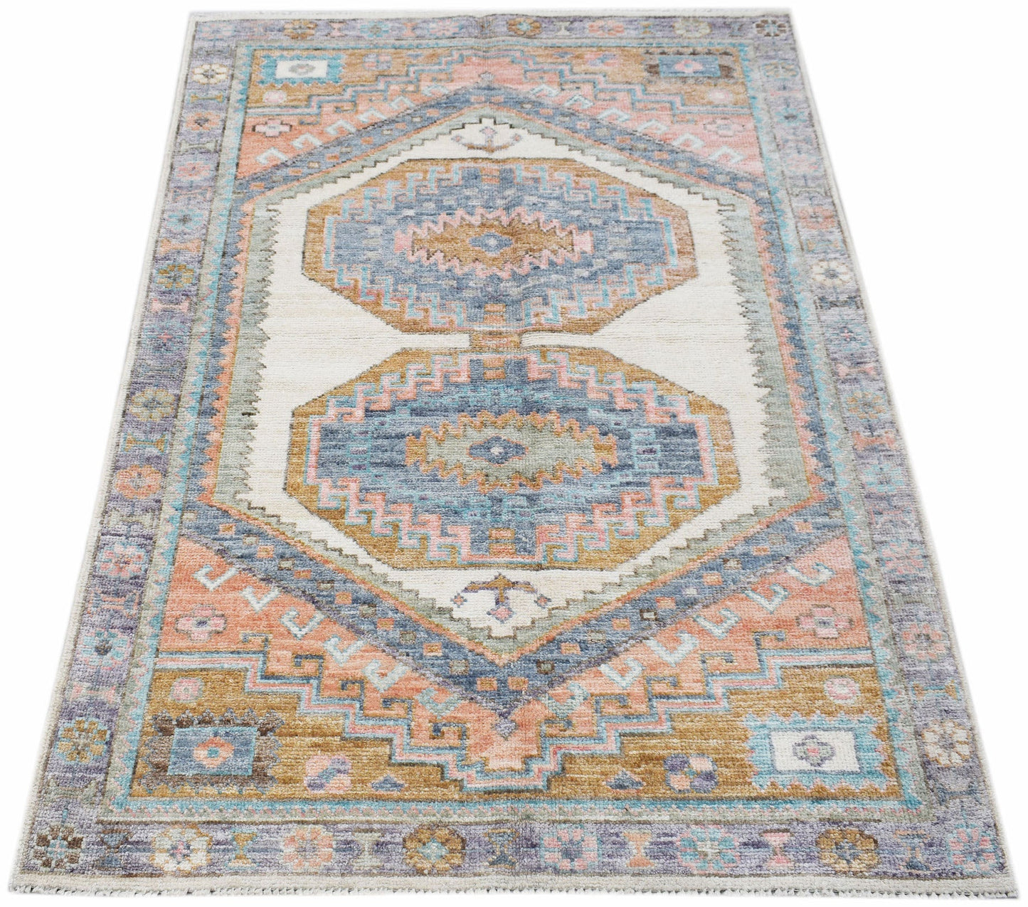 A handwoven transitional Oushak rug featuring geometric patterns in blue, pink, and tan tones.