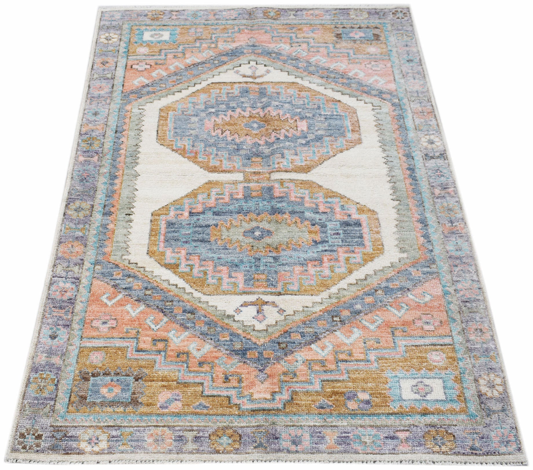 A handwoven transitional Oushak rug featuring geometric patterns in blue, pink, and tan tones.