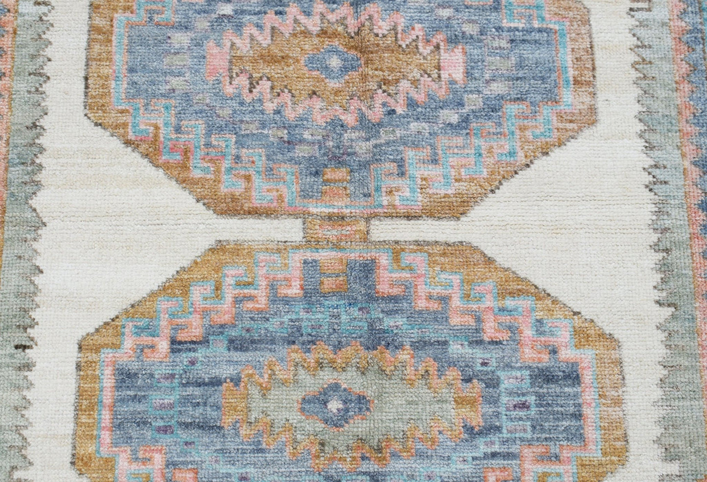 A handwoven Oushak rug featuring geometric medallions in blue, tan, and pink on a cream background.