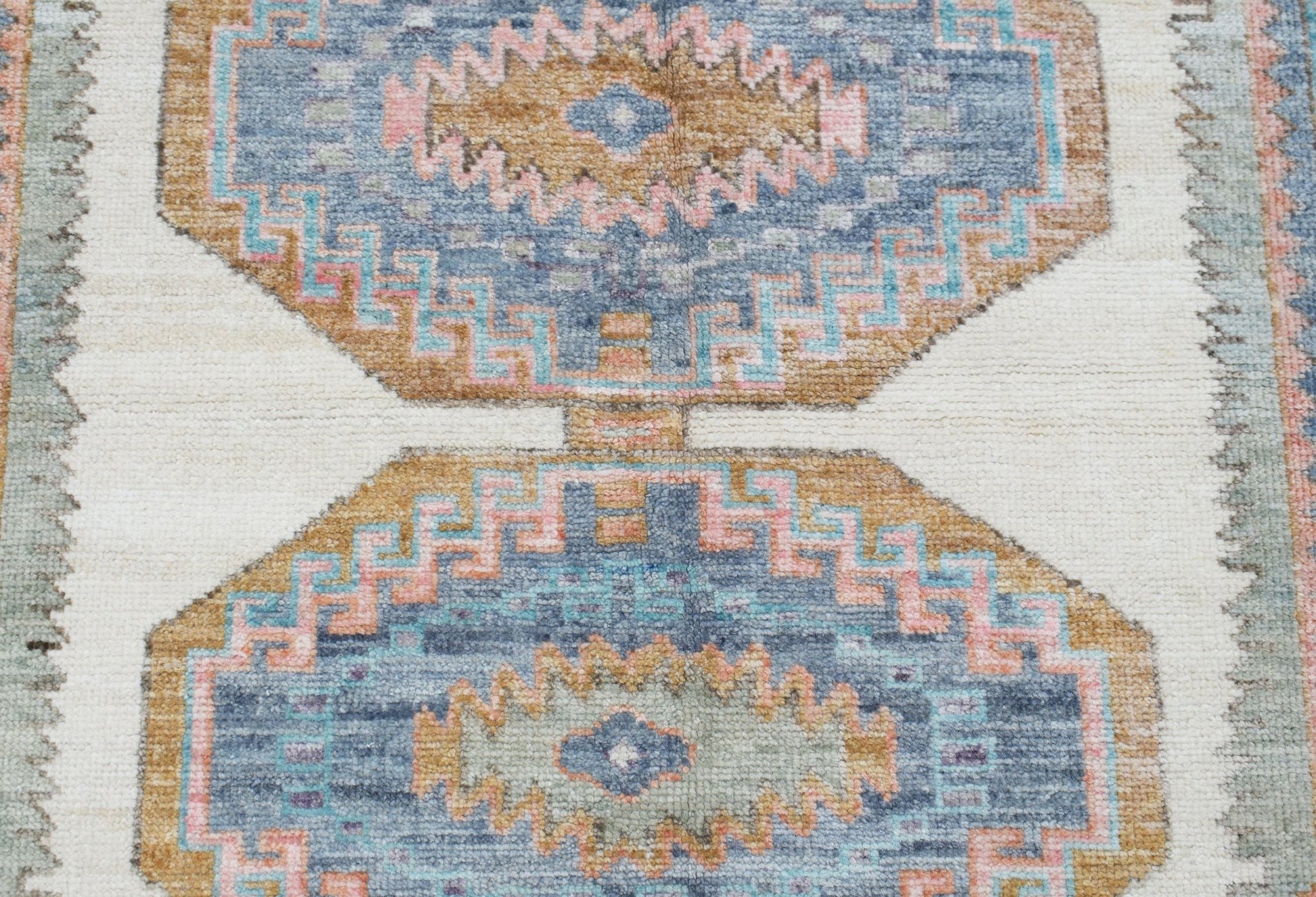A handwoven Oushak rug featuring geometric medallions in blue, tan, and pink on a cream background.