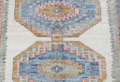 A handwoven Oushak rug featuring geometric medallions in blue, tan, and pink on a cream background.