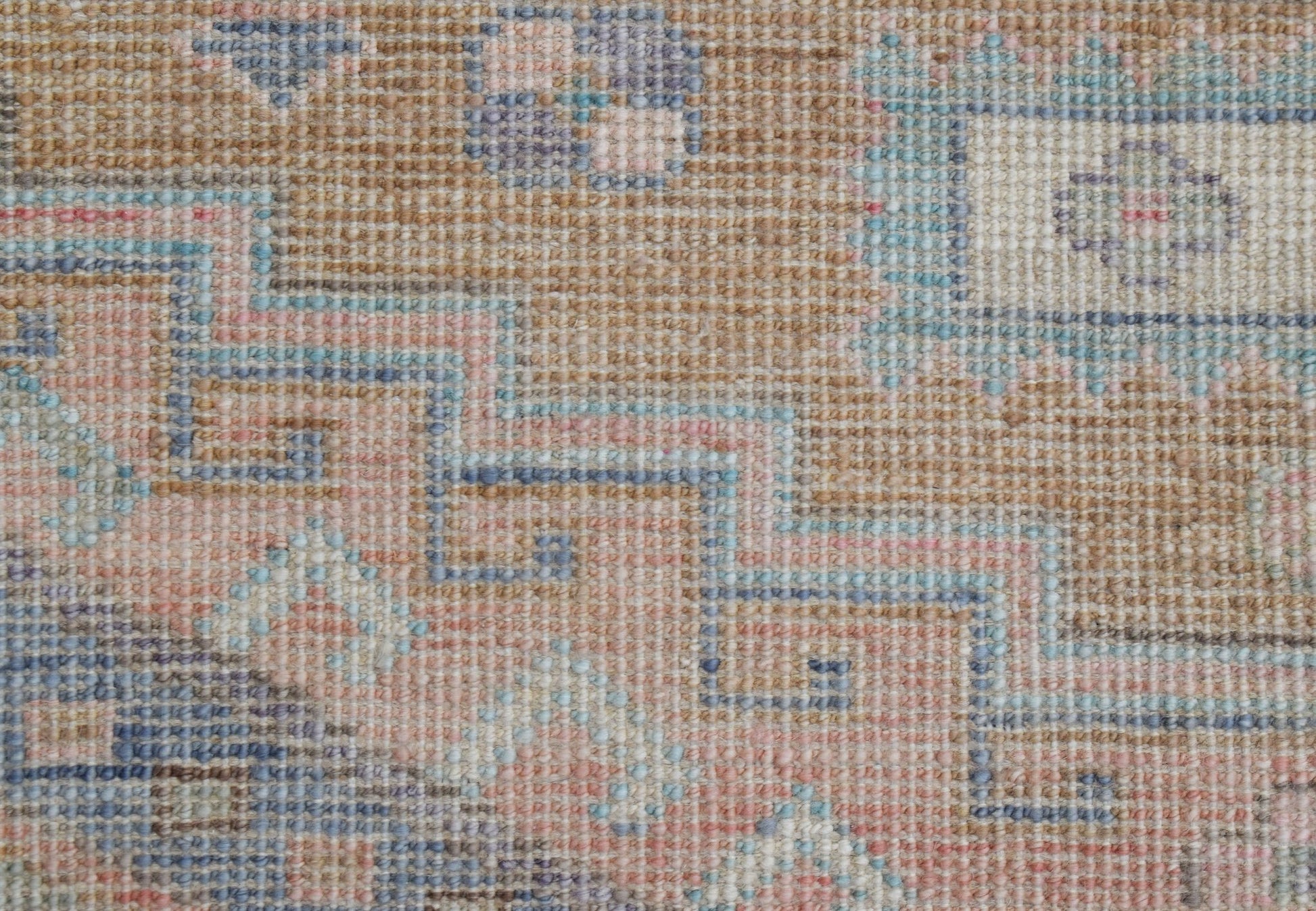 A handwoven transitional Oushak rug featuring a geometric pattern in soft blue, pink, and tan tones.