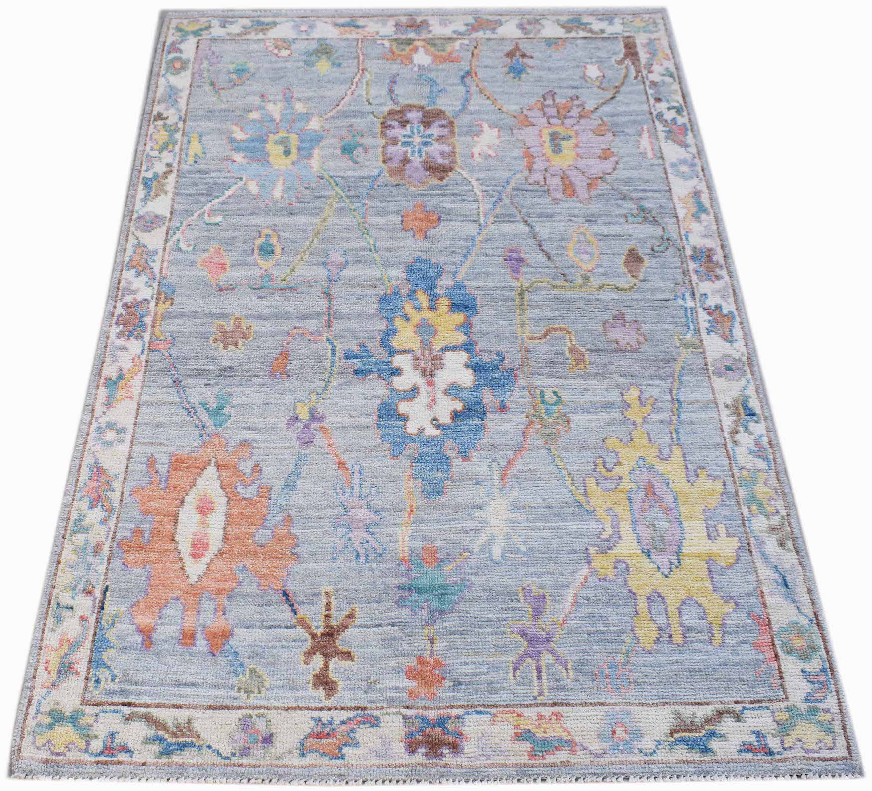 A handwoven transitional Oushak rug featuring a floral pattern in soft colors on a blue background.