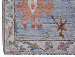 A handwoven transitional Oushak rug featuring a floral pattern in blue, orange, and cream tones.