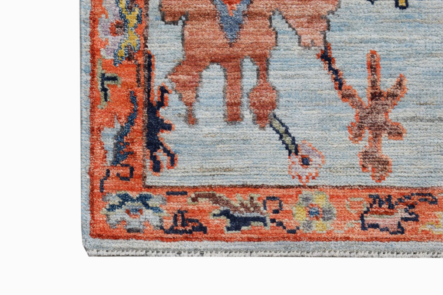A close-up of a handwoven transitional Oushak rug featuring a floral pattern in orange and blue.