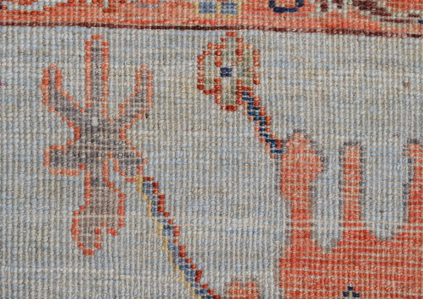 A close-up of a handwoven Oushak rug featuring a light blue field with orange floral motifs.