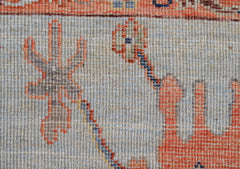 A close-up of a handwoven Oushak rug featuring a light blue field with orange floral motifs.