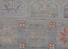 A close-up of a handwoven wool rug featuring a muted, transitional pattern with small orange motifs.