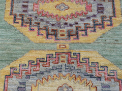 A handwoven wool Oushak rug featuring geometric medallions in yellow, pink, and blue tones.