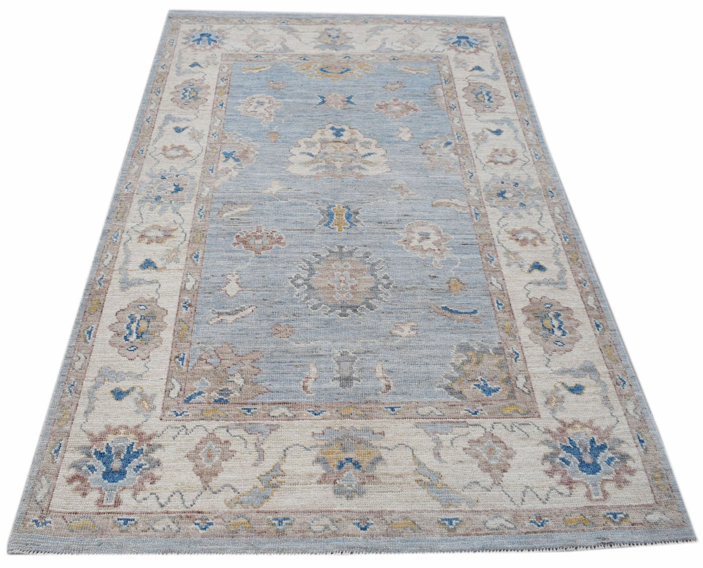 A handwoven transitional Oushak rug featuring a floral pattern in blue, beige, and muted tones.