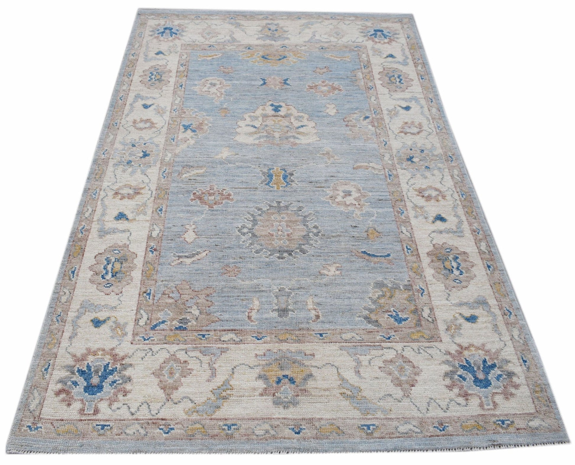 A handwoven transitional Oushak rug featuring a floral pattern in blue, beige, and muted tones.