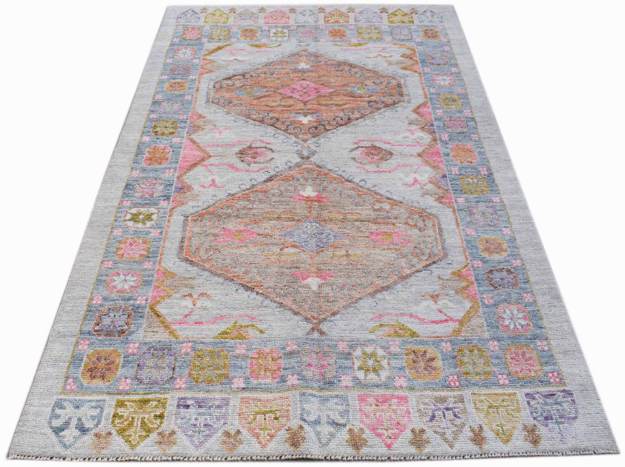 A handwoven transitional Oushak rug featuring a light grey background with pink and tan medallions.