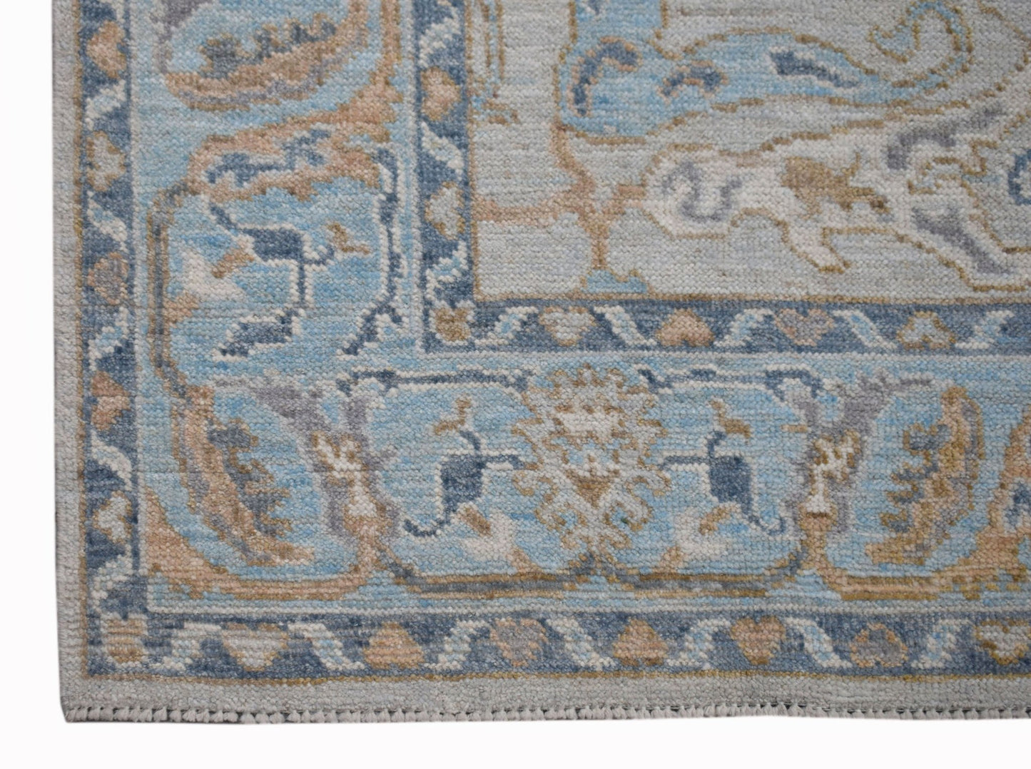 A handwoven transitional Oushak rug featuring a blue and beige floral pattern on a light background.