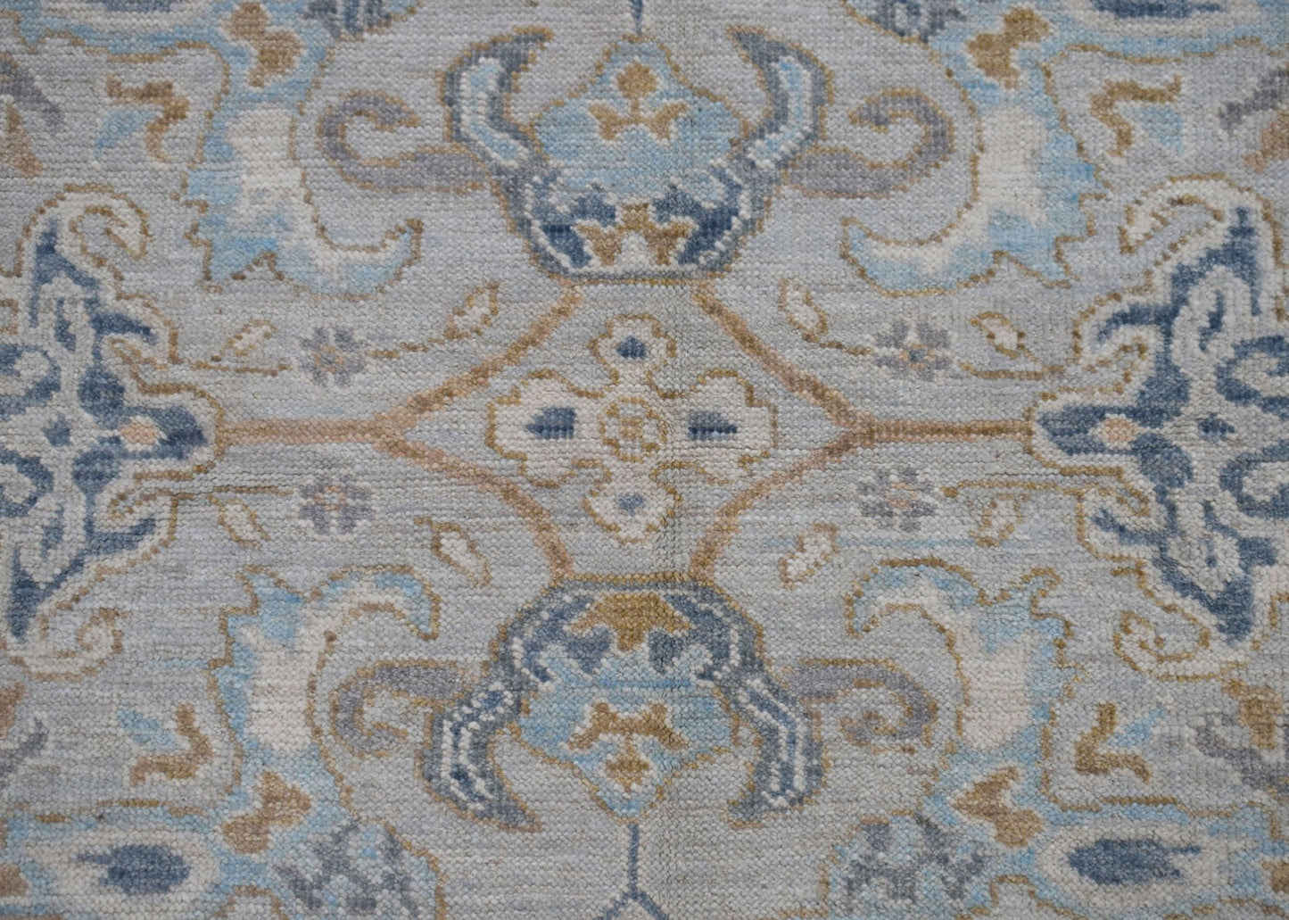A handwoven Oushak rug featuring a transitional floral pattern in shades of blue, grey, and tan.