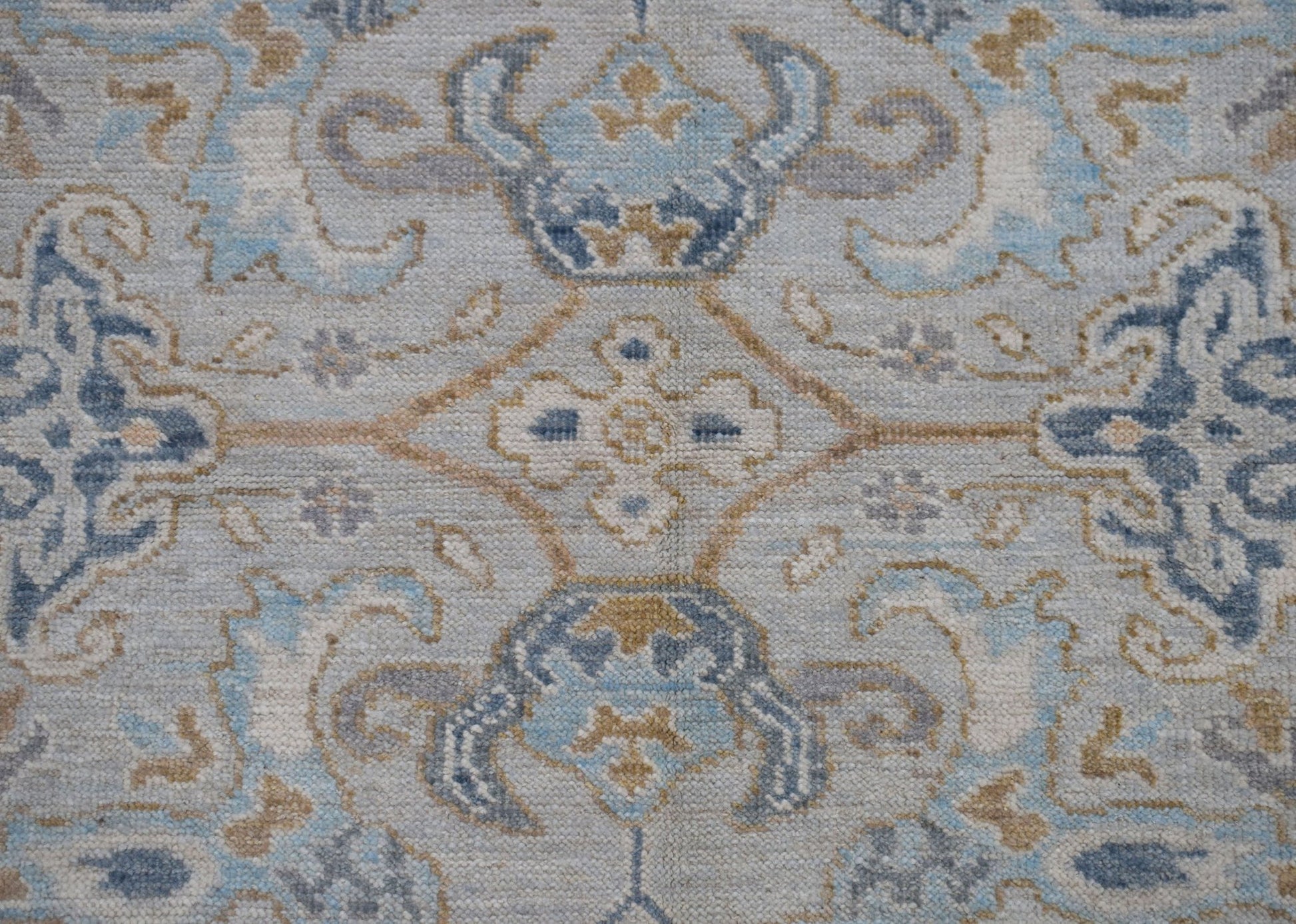A handwoven Oushak rug featuring a transitional floral pattern in shades of blue, grey, and tan.