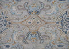 A handwoven Oushak rug featuring a transitional floral pattern in shades of blue, grey, and tan.