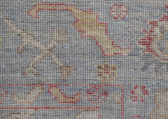 A close-up of a handwoven Oushak rug featuring a floral pattern in muted blue, red, and gold tones.