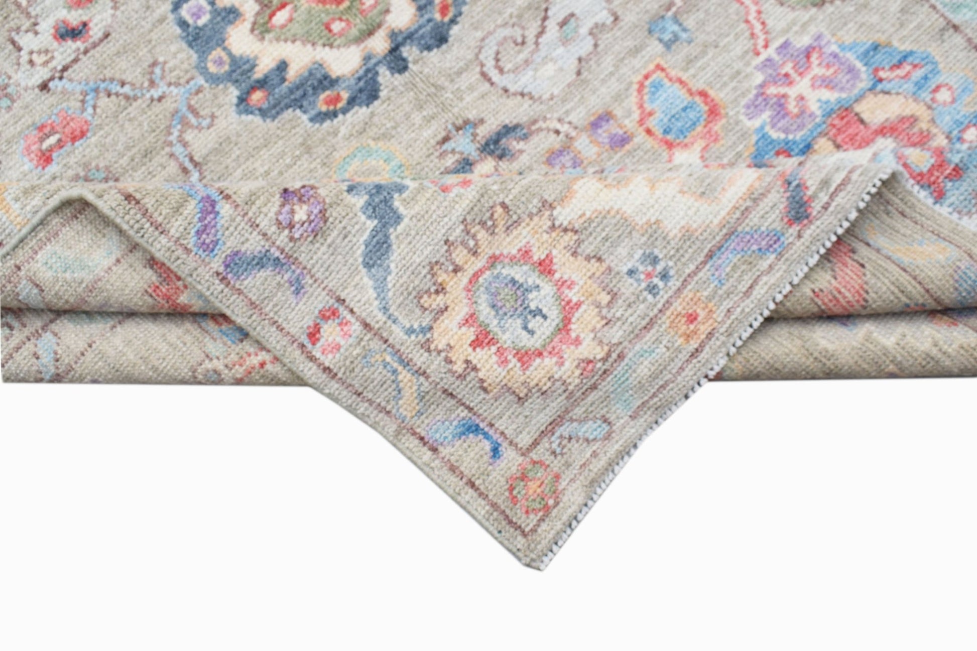 A handwoven transitional Oushak rug with a floral pattern in muted tones on a light grey background.