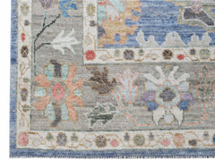 A transitional Oushak rug featuring a floral pattern in muted tones on a grey background.