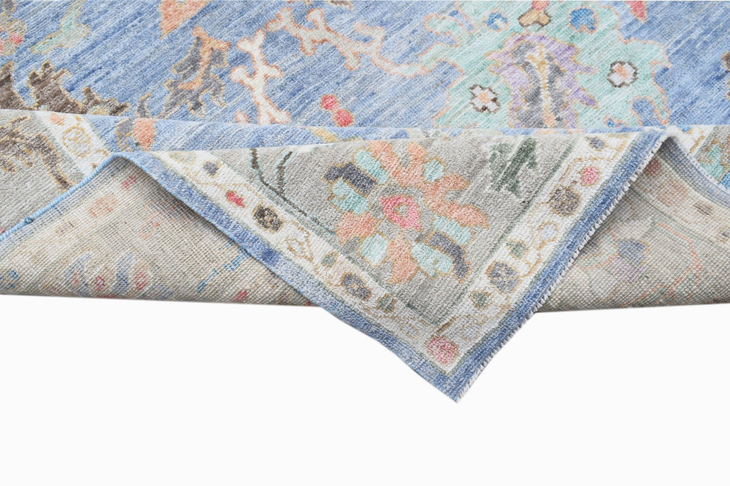 A handwoven transitional Oushak rug with a blue floral pattern and a folded corner.