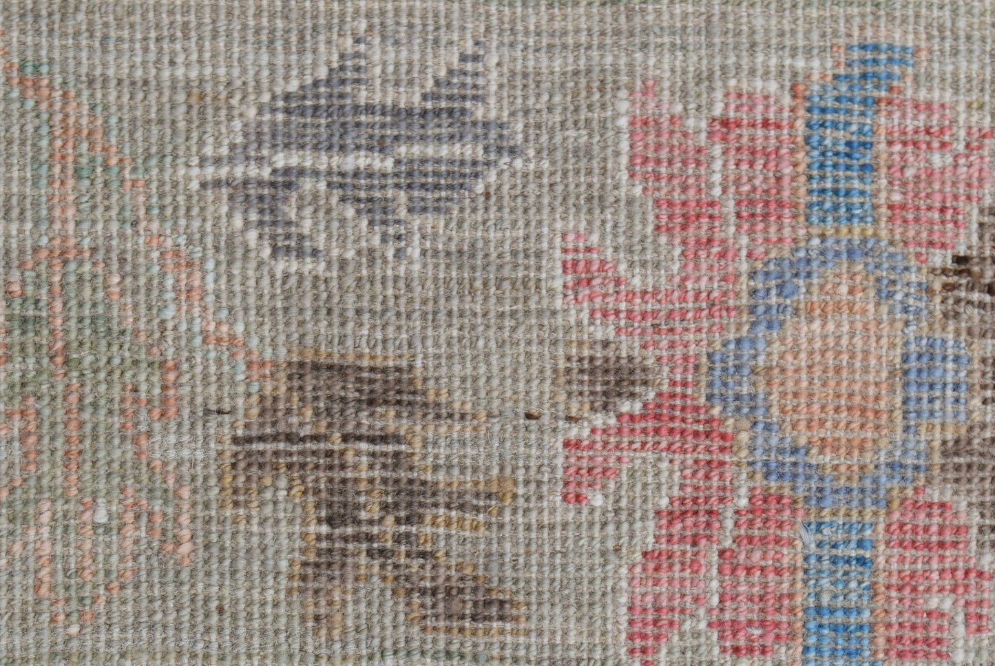 A close-up view of a handwoven Oushak rug featuring a floral pattern in muted tones.