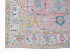 A handwoven transitional Oushak rug featuring a floral pattern in pink, blue, and yellow tones.