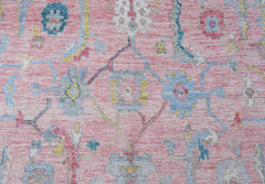 A handwoven transitional Oushak rug featuring a floral pattern in soft pink, blue, and yellow tones.