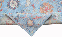 A handwoven transitional Oushak rug featuring a floral pattern in blue, orange, and cream tones.