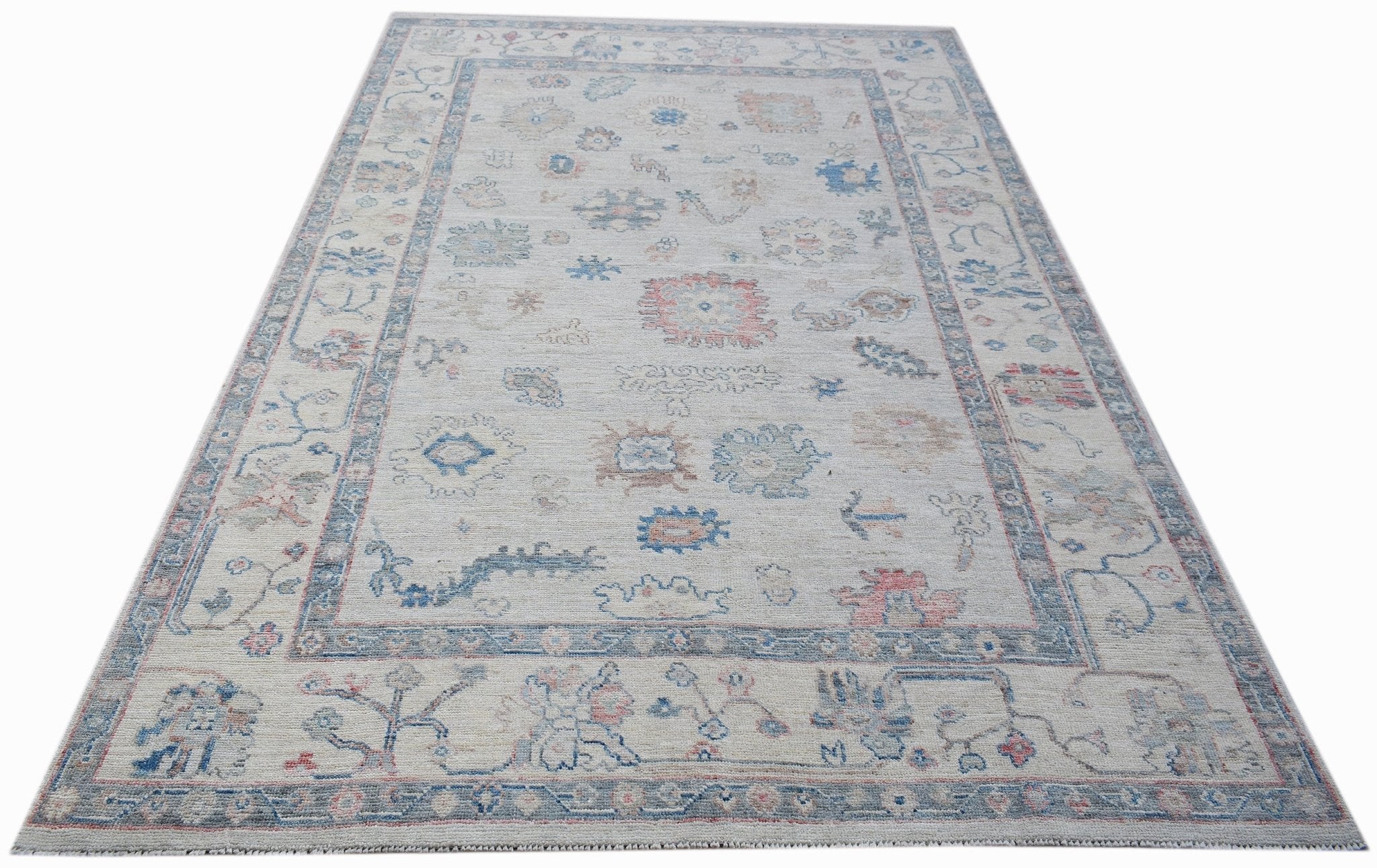 A handwoven transitional Oushak rug featuring a floral pattern in soft blue and pink tones.