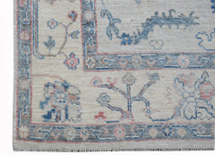 A handwoven transitional Oushak rug featuring a floral pattern in blue and pink on a cream field.