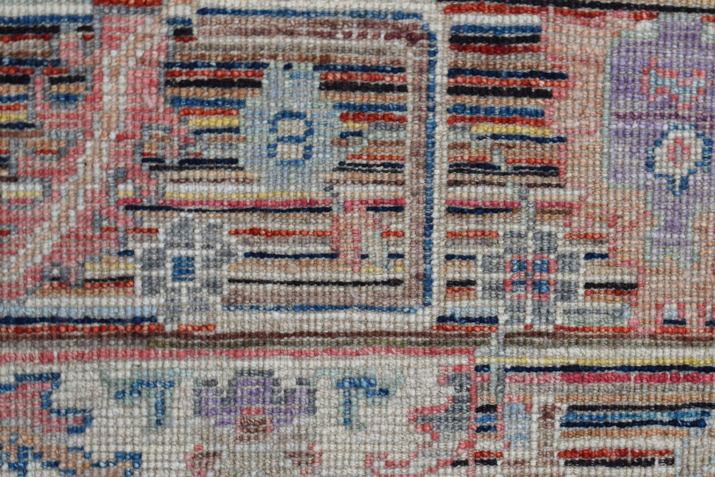 A close-up of a handwoven wool rug featuring a geometric pattern in muted, transitional colors.