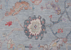 A handwoven transitional Oushak rug featuring a floral pattern in muted tones on a blue background.