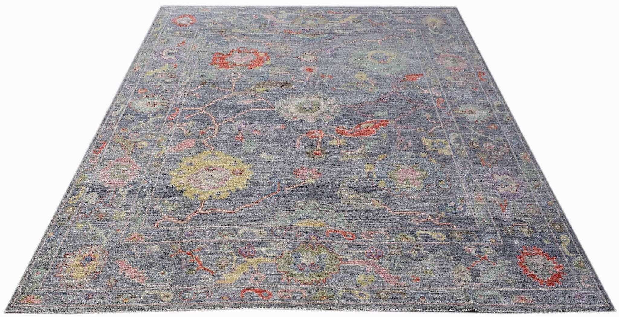 A handwoven transitional Oushak rug featuring a floral pattern in muted tones on a blue background.