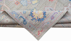 A handwoven transitional Oushak rug with a floral pattern in blue, yellow, and pink on a beige base.