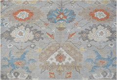 A handwoven transitional Oushak rug featuring a floral pattern in muted blue, orange, and tan tones.