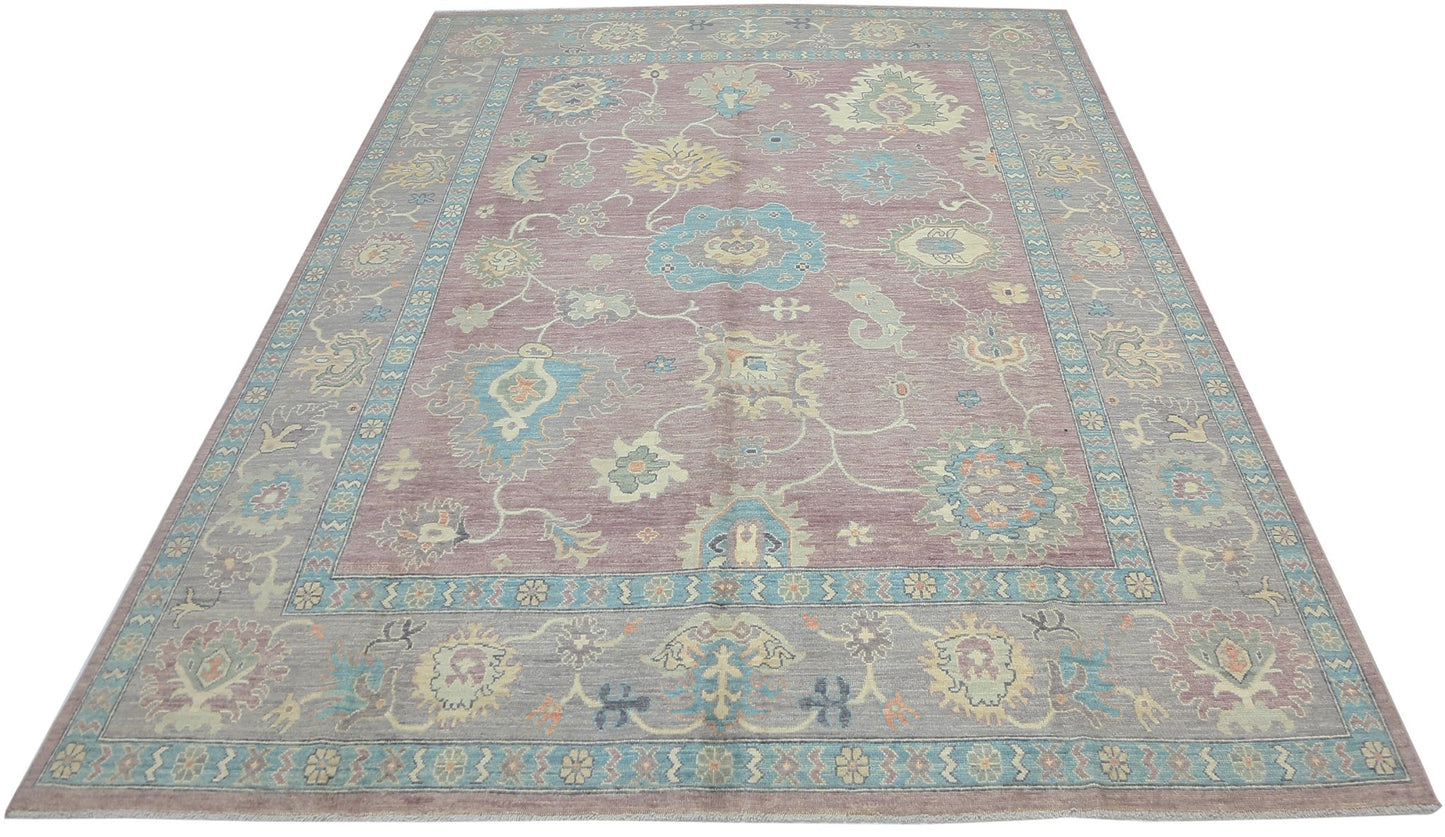 A handwoven transitional Oushak rug featuring a floral pattern in muted tones on a mauve background.