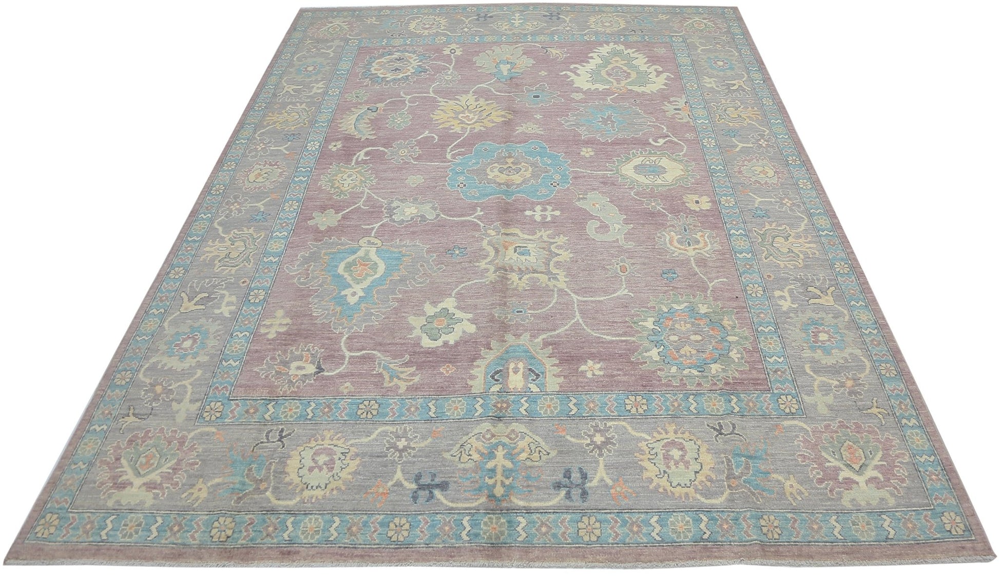 A handwoven transitional Oushak rug featuring a floral pattern in muted tones on a mauve background.