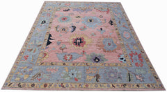 A transitional Oushak rug featuring a floral pattern in muted tones on a pink field.