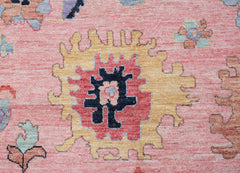 A handwoven transitional Oushak rug featuring a central floral medallion in pink, yellow, and blue.