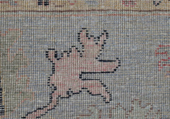 A close-up of a handwoven wool rug featuring a stylized pink animal motif on a blue background.
